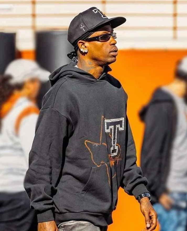Man wearing a black graphic hoodie, cap, and sunglasses outdoors