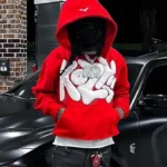 Person wearing a red graphic hoodie with a pointed hood beside a black car.