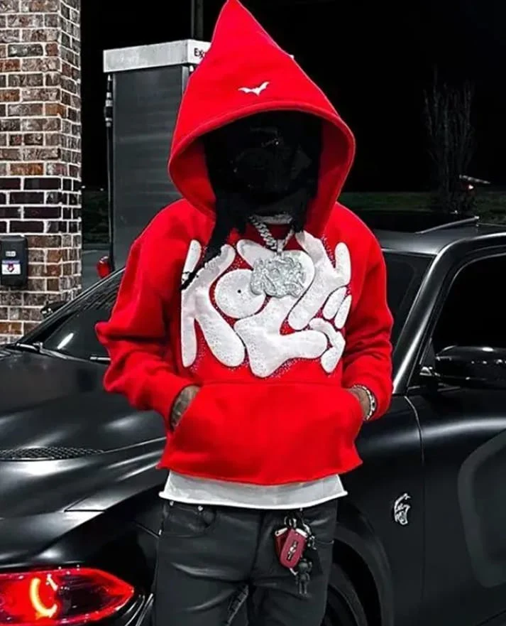 Person wearing a red graphic hoodie with a pointed hood beside a black car.